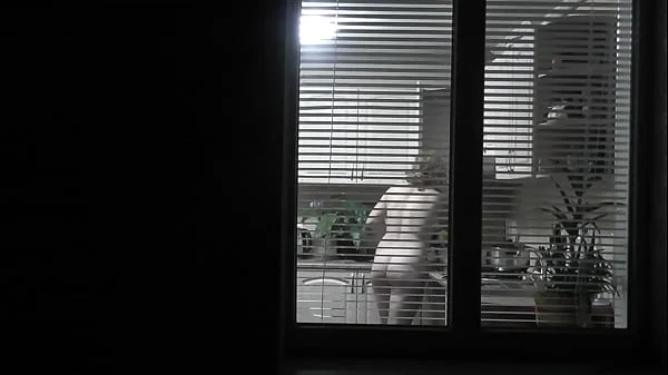 Peeping. Voyeur. Neighbor pervert voyeur in evening on street looks out window as naked sexy neighbor in kitchen prepares dinner for her husband. Naked in public. Naked at home. Family. Outdoor